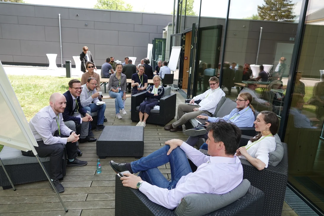 Mehrere Personen sitzen auf einer Terrasse und diskutieren.
