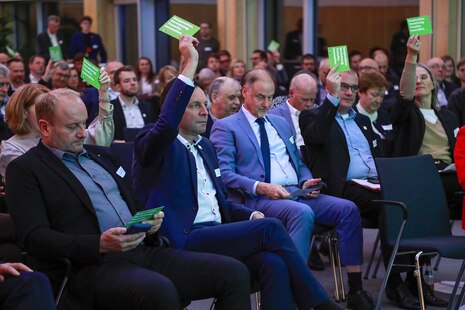Teilnehmer des Zukunftsforums sitzen auf ihren Stühlen und halten grüne Karten in die Luft.