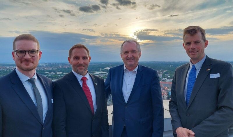 Mehrere Personen stehen auf einer Dachterrasse vor einem Sonnuntergang