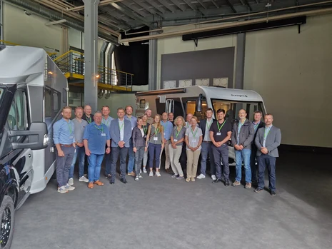 Eine Gruppe von Menschen steht in einer Halle zwischen zwei Wohnmobilen