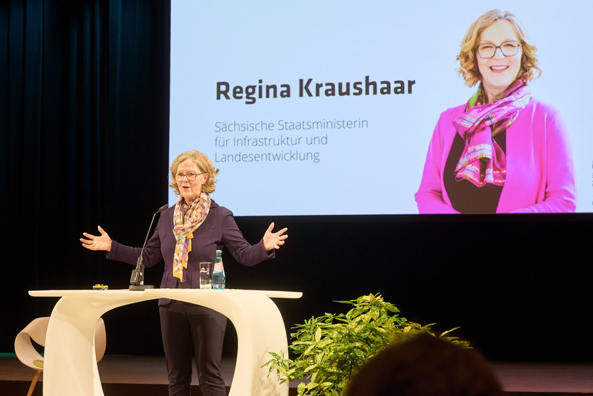 Ministerin Kraushaar steht an einem Rednerpult und hält eine Rede. Im Hintergrund ist eine Leinwand zu sehen.