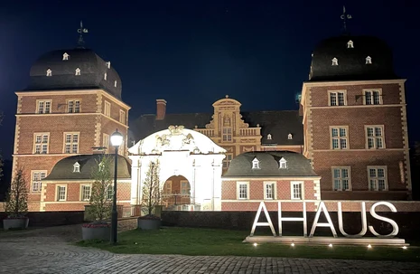 Blick bei Nacht auf ein Schloss welches beleuchtet ist und der Schriftzug Ahaus davor aufgestellt wurde.