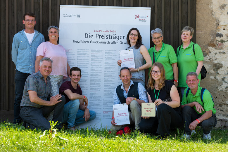 Mehrere Personen stehen vor einer Leinwand mit der Aufschrift Die Preisträger und halten Urkunden in der Hand.
