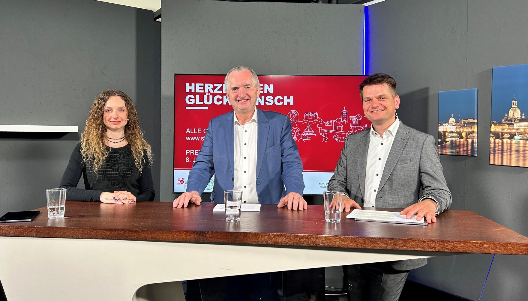 Staatsminister Schmidt und zwei weitere Personen stehen an einem Tisch und schauen in die Kamera