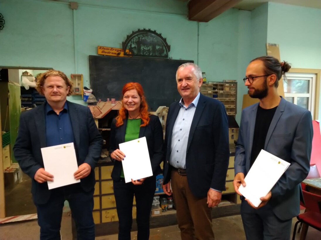 4 Personen posieren für ein Foto. 3 Personen halten ein Blatt Papier in der Hand.