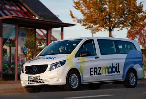 Ein weißer Kleinbus steht an einer Haltestellt. Er trägt den Schriftzug "Erzmobil" auf der Seite.