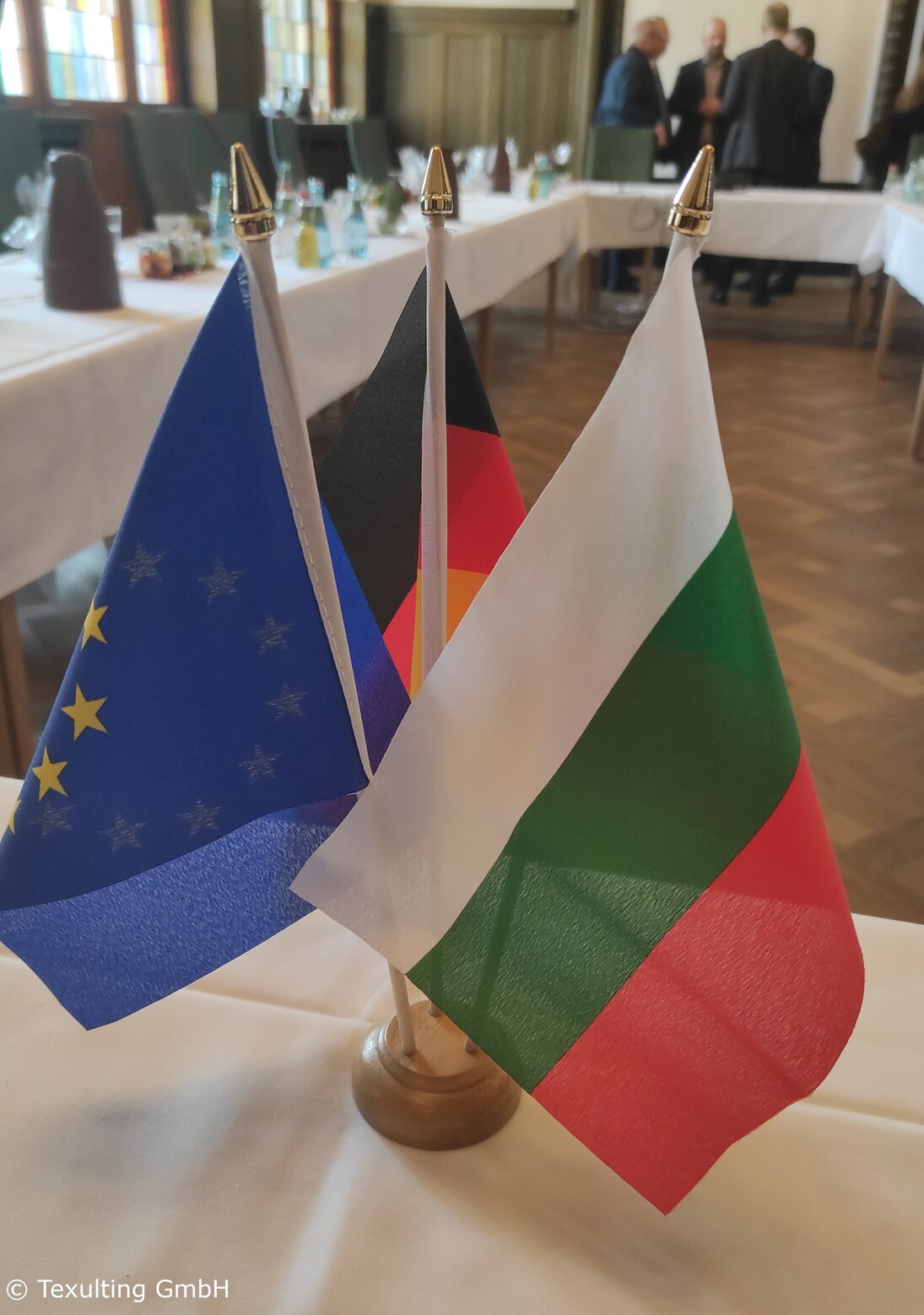 Auf einem Tisch stehen eine bulgarische, eine deutsche und eine Flagge der Europäischen Union