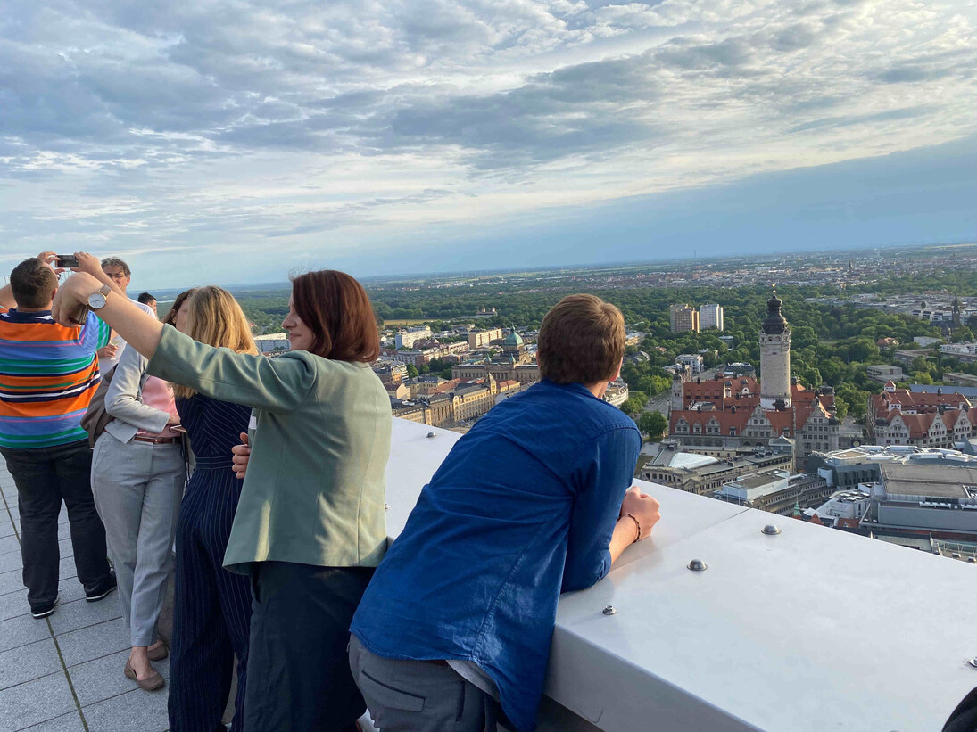 Menschen stehen auf einer Dachterrasse mit Blick auf Leipzig