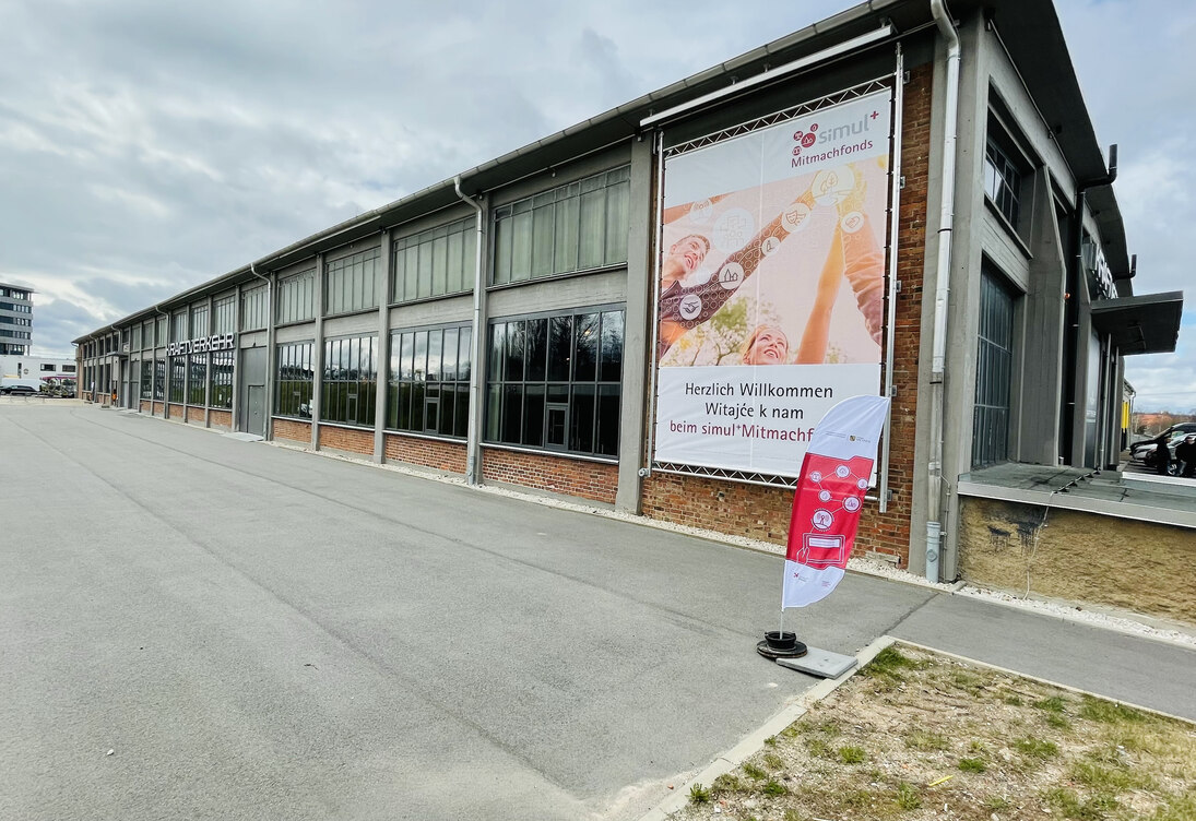 Veranstaltungshalle von außen mit simul+ Mitmachfonds Banner an der Außenfassade