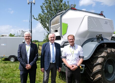 Drei Männer stehen vor einem Landwirtschaftsroboter