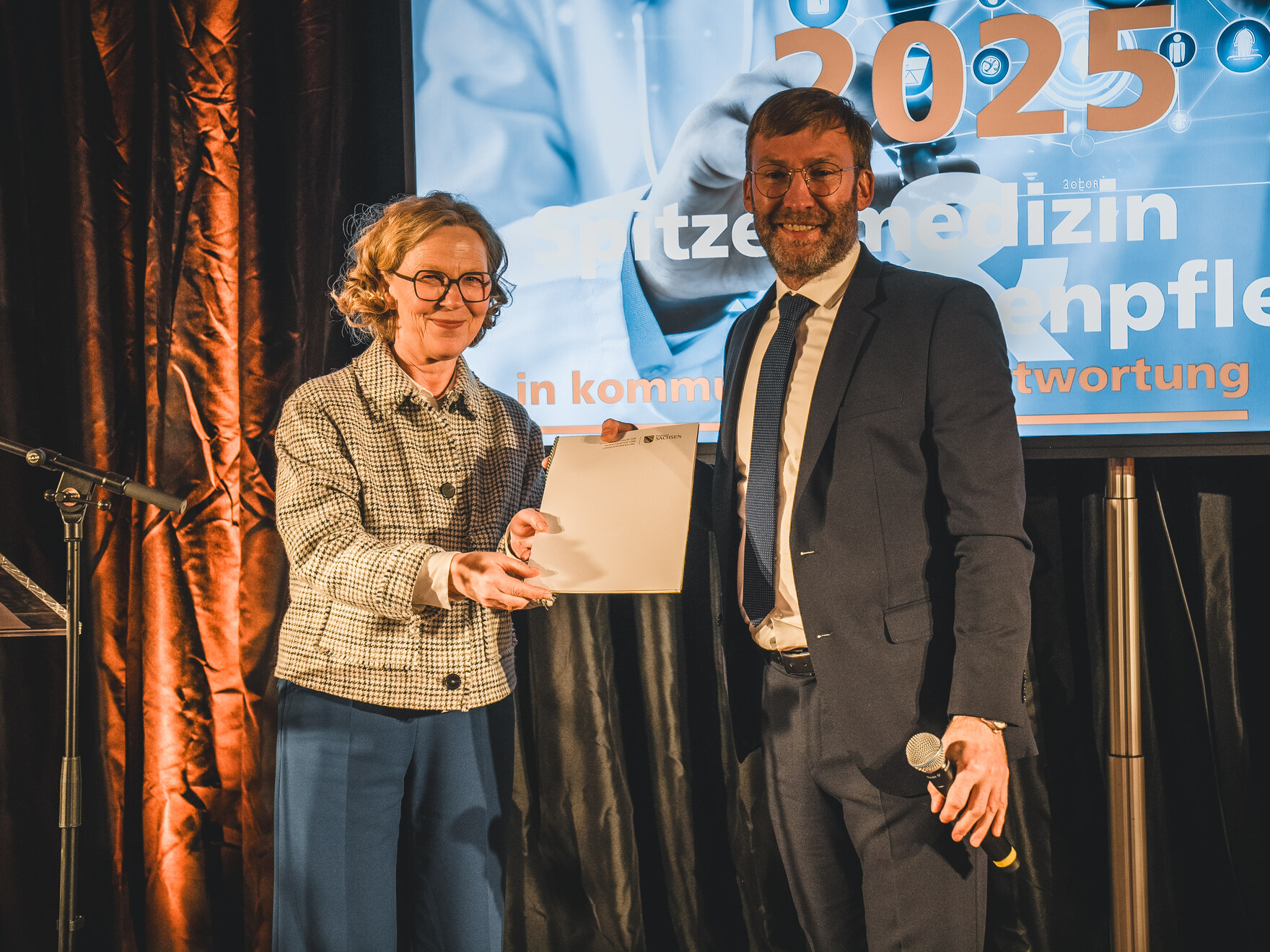 Staatsministerin Kraushaar übergibt Herrn Scharfenberg eine Mappe.