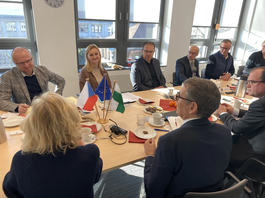 Mehrere Personen sitzen an einem langen Tisch und unterhalten sich.