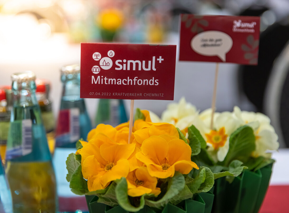 Ein kleiner gelber Blumentischschmuck mit simul+ Mitmachfonds Fähnchen 