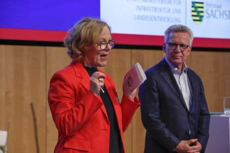 Ministerin Kraushaar steht gemeinsam mit Thomas de Maiziére auf der Bühne und sie spricht zum Publikum