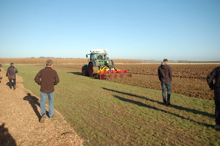 Ein Traktor mit Pfluggerät fährt über ein Feld. Daneben stehen mehrere Menschen.